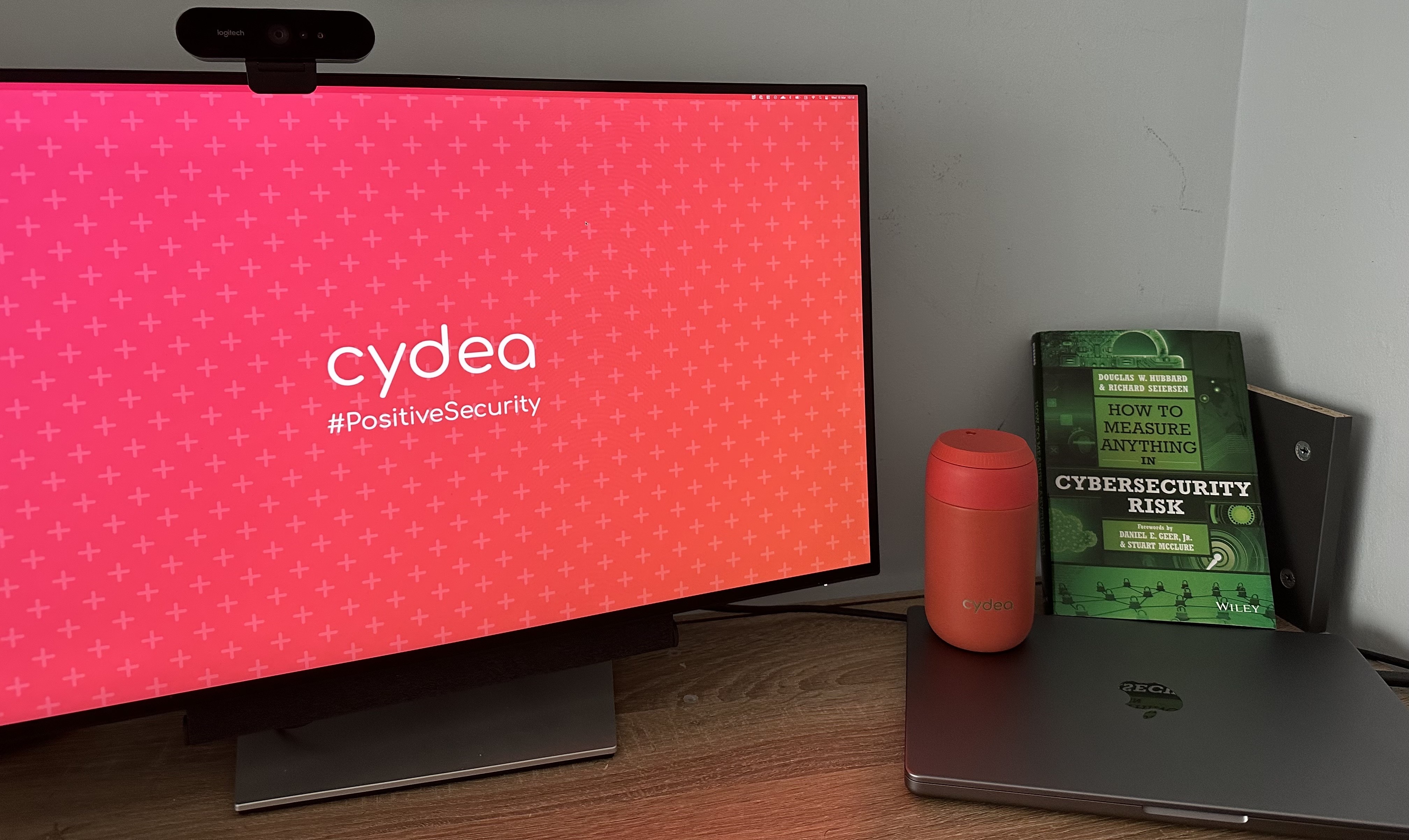 Image of desk with travel mug, book and Cydea branded background on screen