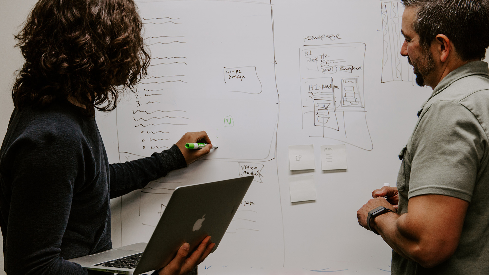 decorative: two people standing at a whiteboard discussing designs