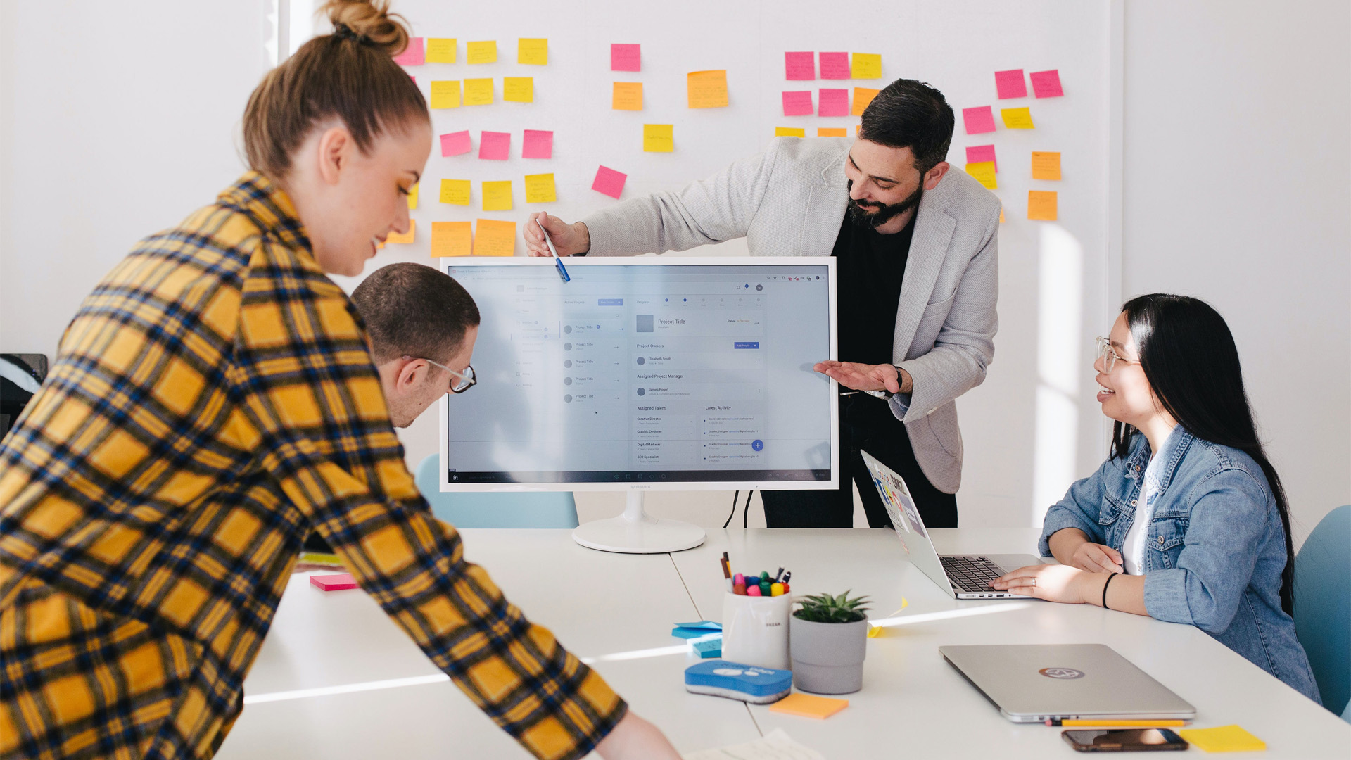 decorative: group of people working together on a monitor and whiteboard with post it notes